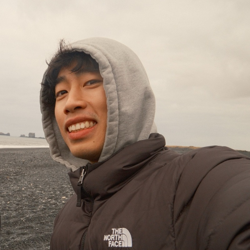 Minh smiling in a hoodie at a beach